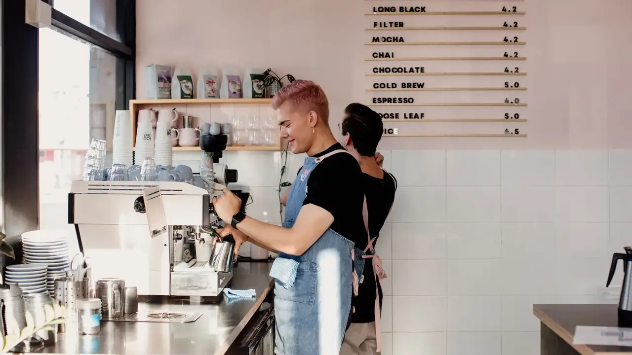 Baristas preparing coffee behind the counter at a modern Newcastle café with menu board and espresso machine.