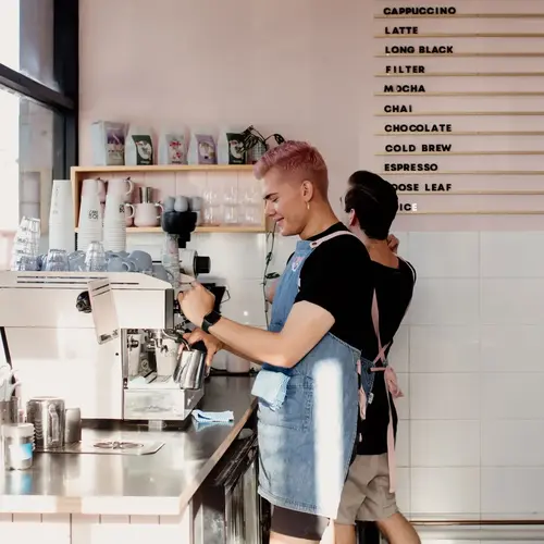 Baristas preparing coffee behind the counter at a modern Newcastle café with menu board and espresso machine.