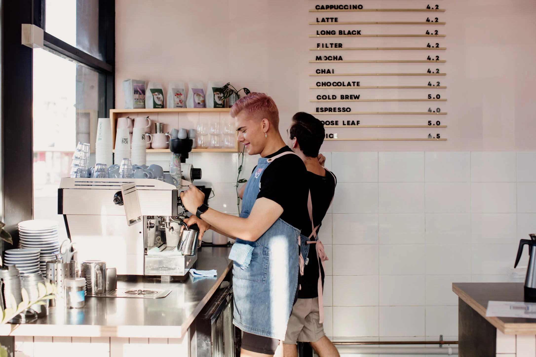 Baristas preparing coffee behind the counter at a modern Newcastle café with menu board and espresso machine.
