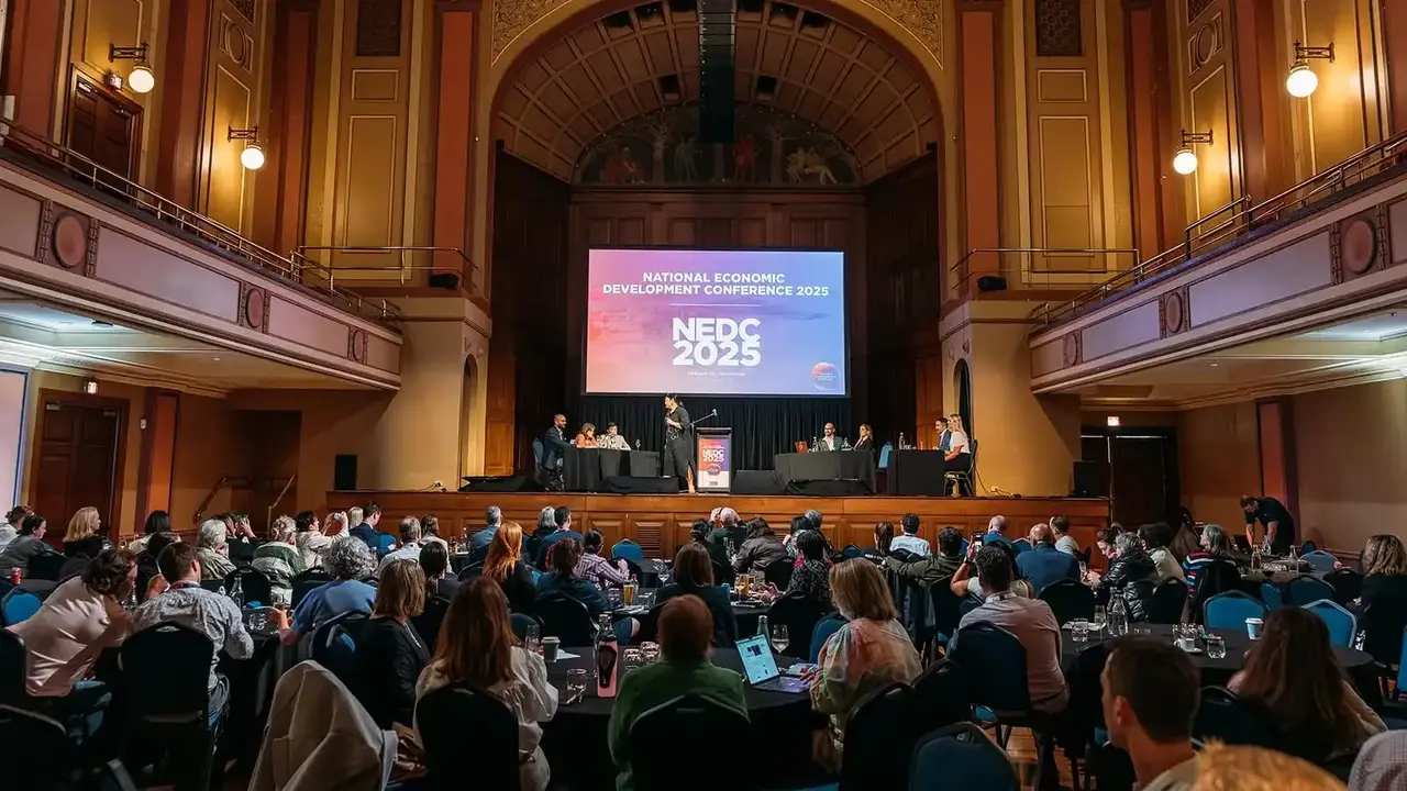 View across delegates seated at round tables looking towards speakers presenting on stage in front of an Economic Development Australia banner at Newcastle City Hall.