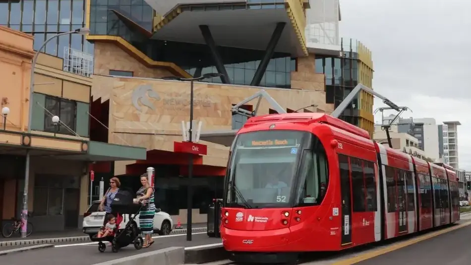 A red tram arrives at Civic light rail stop outside Civic Theatre Newcastle and the University of Newcastle. 