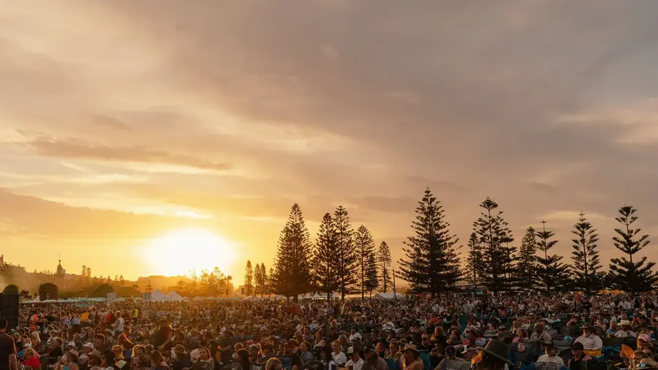 Large crowd at Howlin Country music festival in Newcastle’s Foreshore Park during sunset with tall trees in the background.
