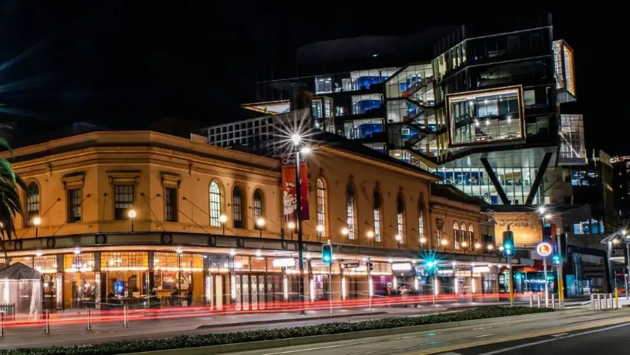 Civic Theatre Newcastle at night with illuminated clock tower, palm trees, and modern buildings in the background.