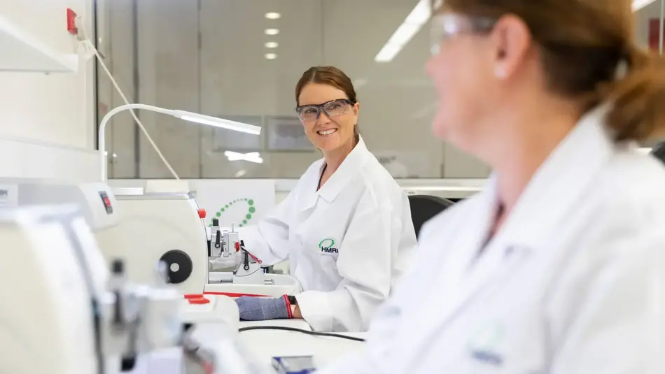 Researchers in lab coats operating precision equipment inside a bright laboratory at HMRI Newcastle.