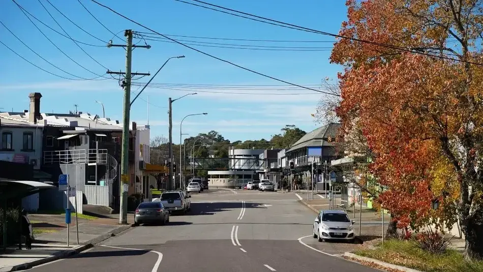 Street view of Wallsend town centre with shops, cars, and autumn trees under clear blue sky.