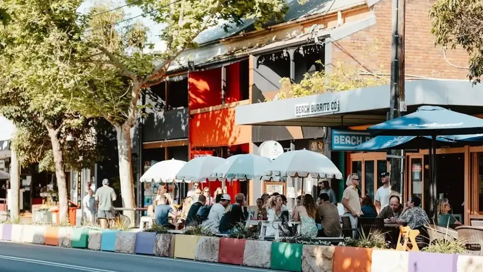 Outdoor dining along Darby Street in Newcastle with colourful barriers, umbrellas, and people enjoying food and drinks.