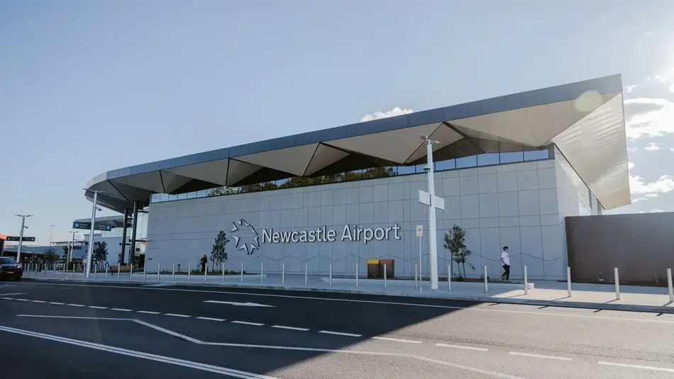 Newcastle Airport's new terminal entrance with angular rooflines, glass panels, and bold signage on a clear day.