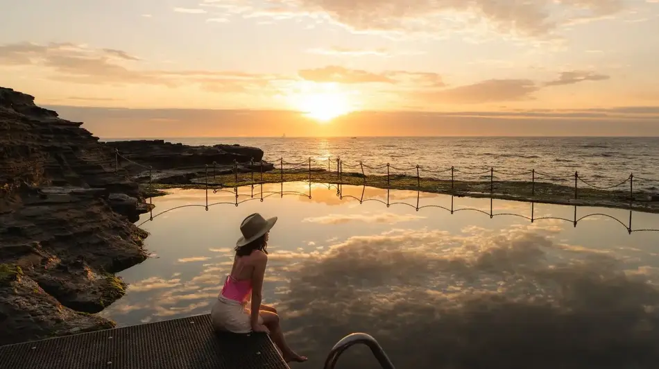 Female sitting with feet in the water watching the sun rise over the Newcastle Bogey Hole. 
