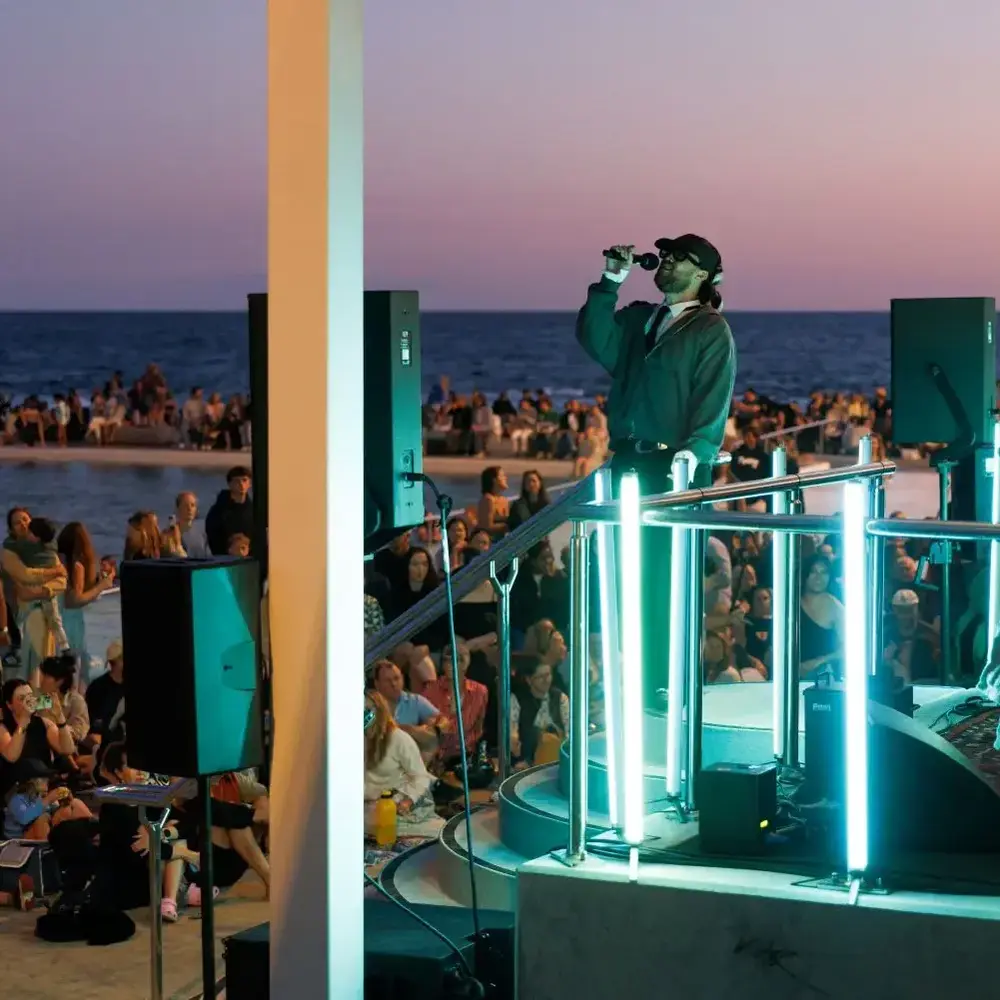 Live music performance at Newcastle Ocean Baths during sunset for New Annual festival with crowd by the water.