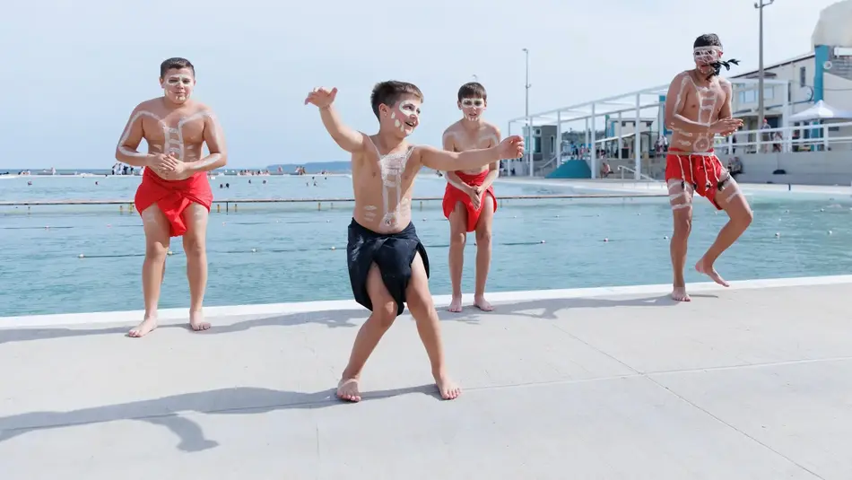 Young performers showcase traditional dance at Newcastle Ocean Baths during New Annual festival, with ocean pool in the background.